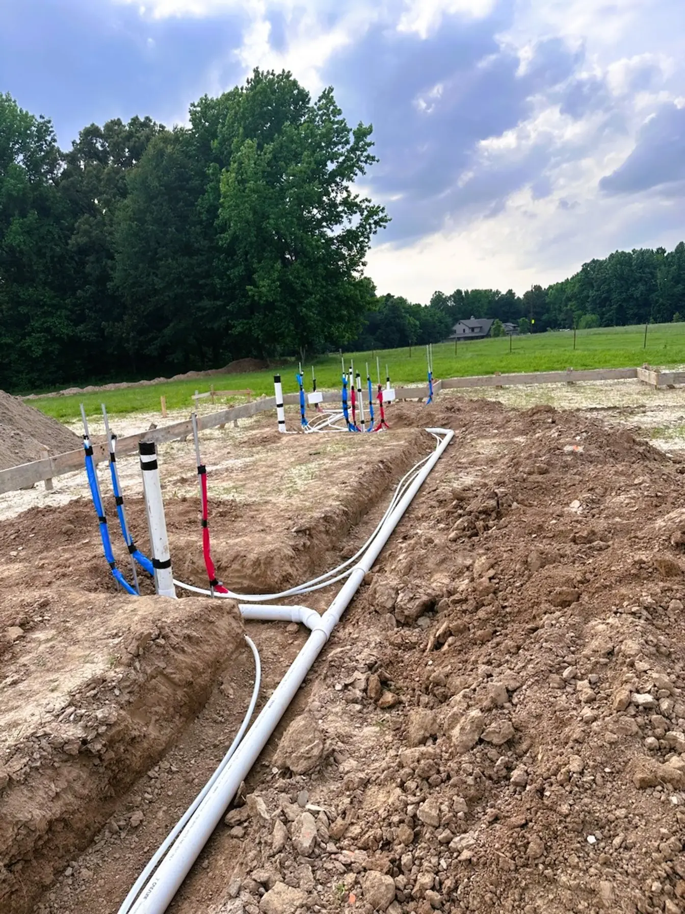 Underground plumbing rough-in laid out in trenches inside foundation form boards on a rural lot