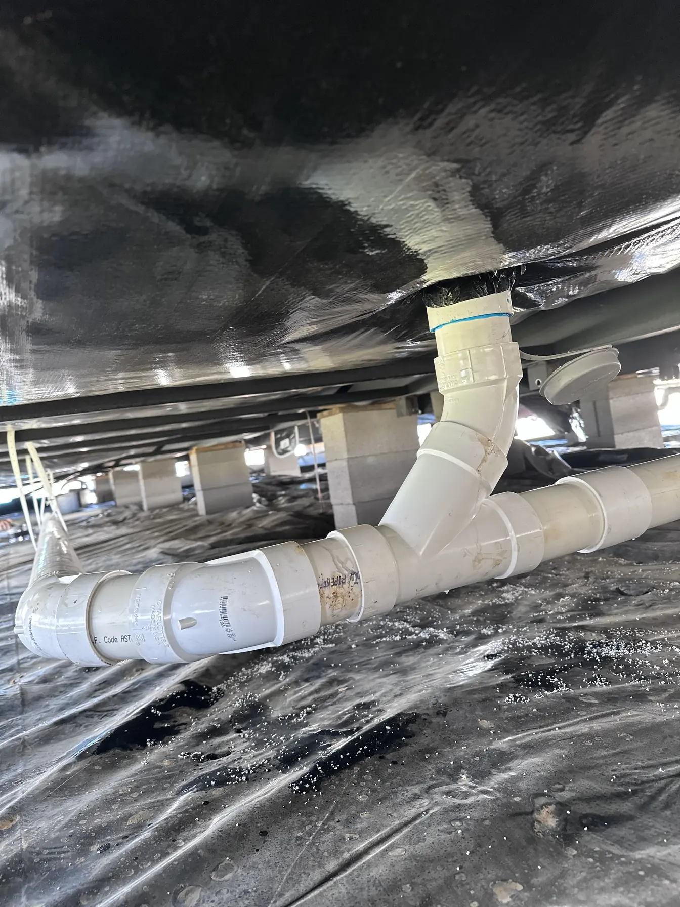 New white PVC drain lines hung and sloped beneath a home