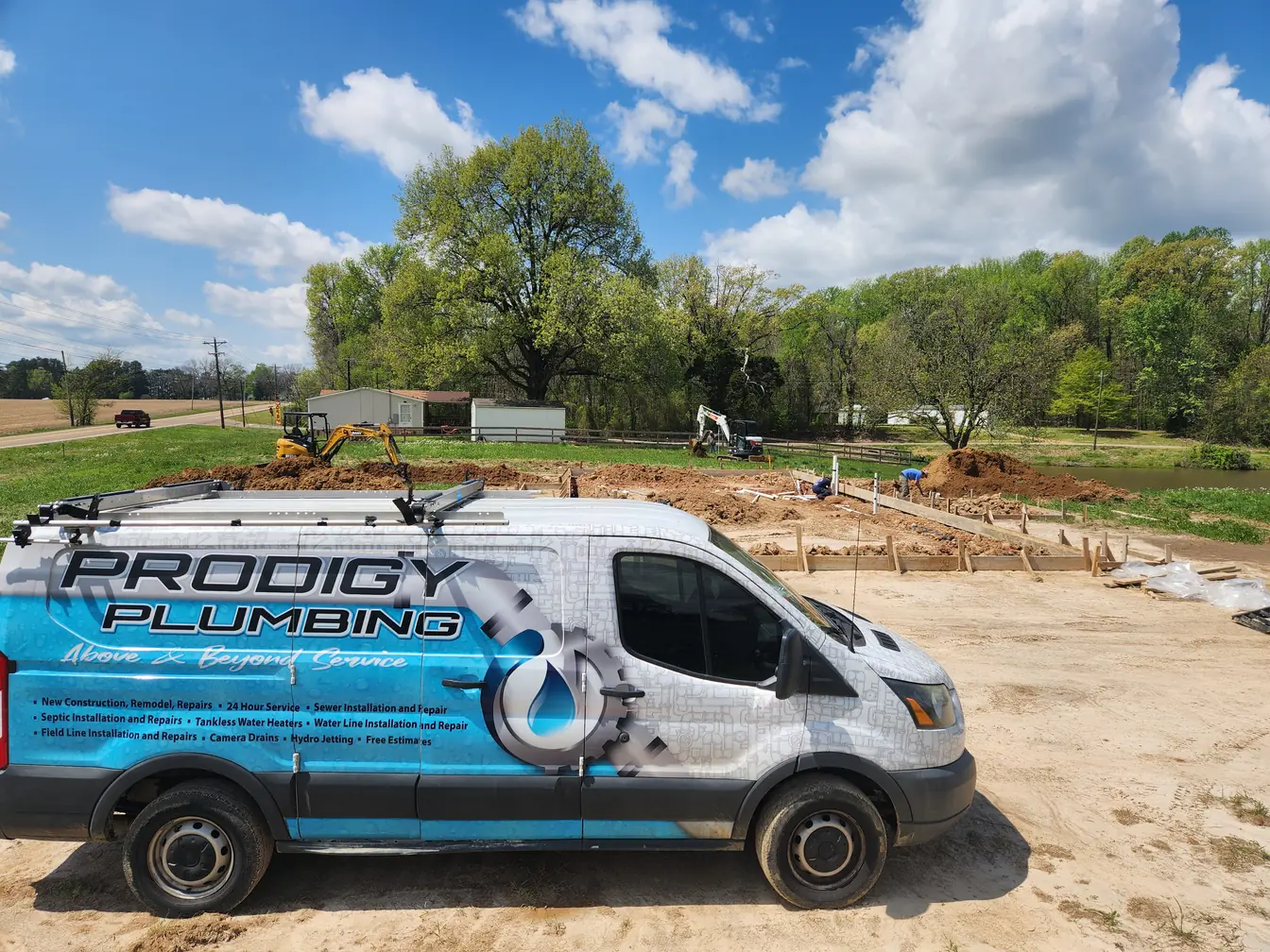 Prodigy Plumbing wrapped service van parked at a new-construction site with an excavator and slab forms behind it