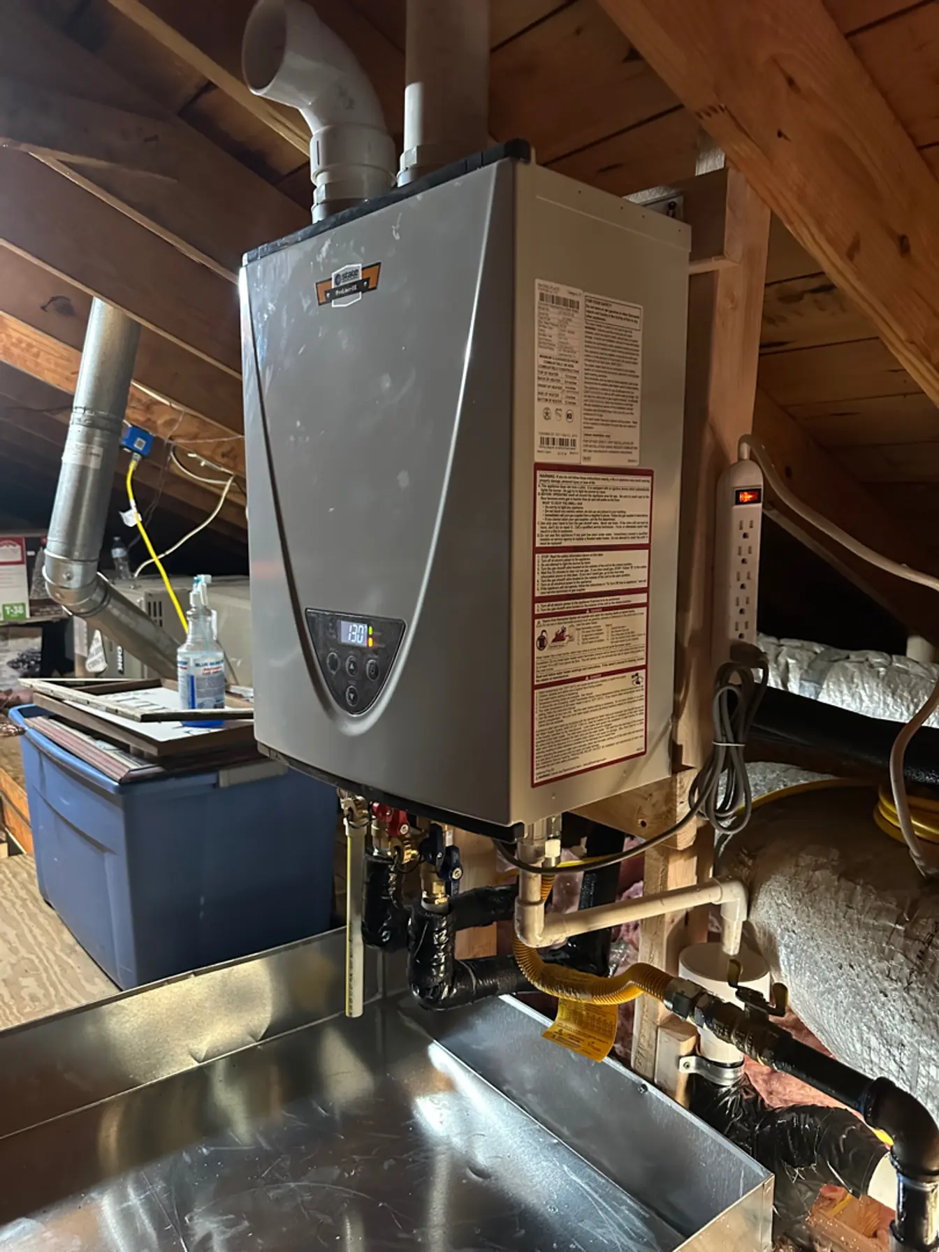 Wall-hung tankless water heater installed in an attic with isolation valves and gas flex connected